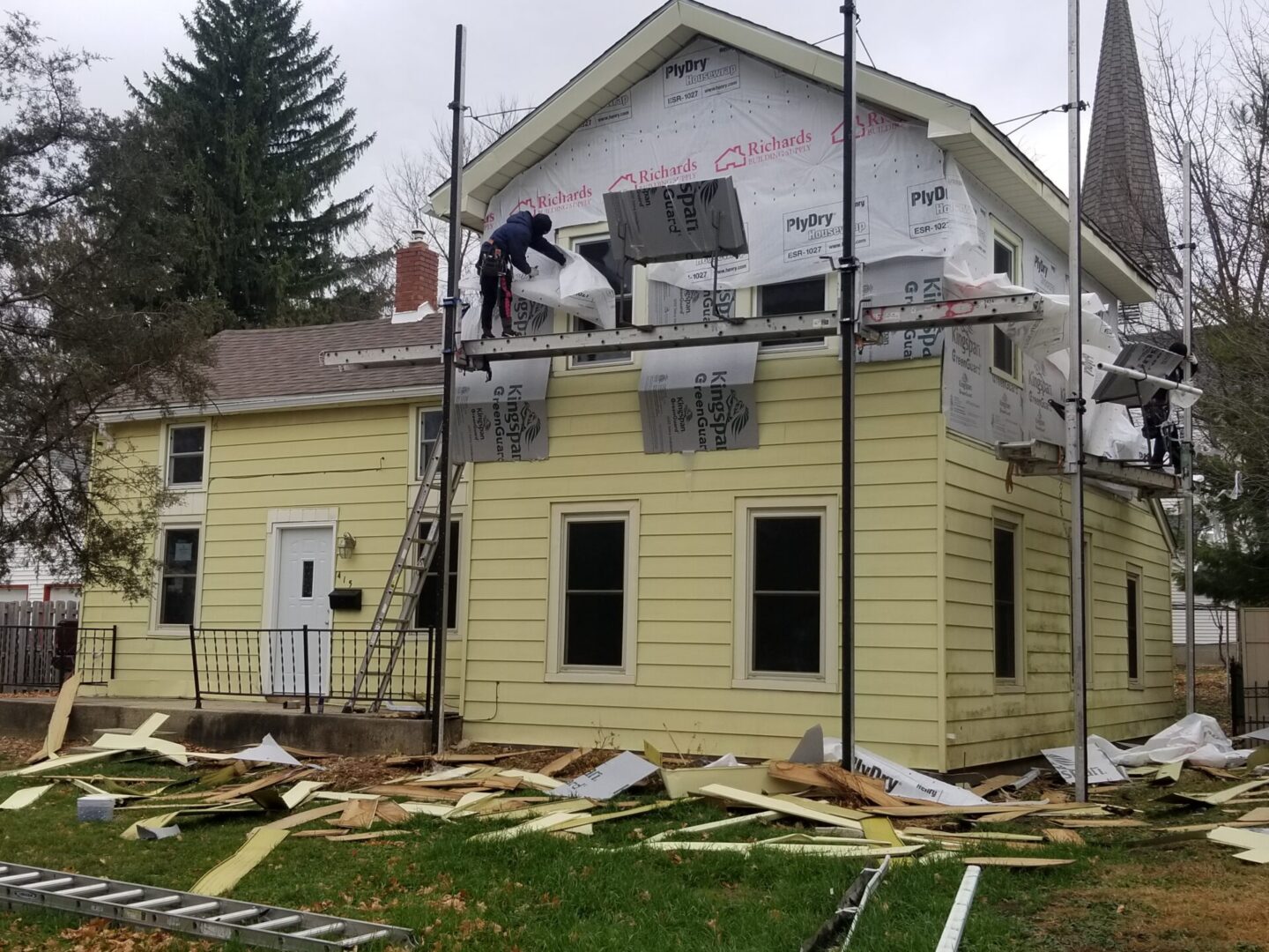 A man on a ladder working on the roof of a house.